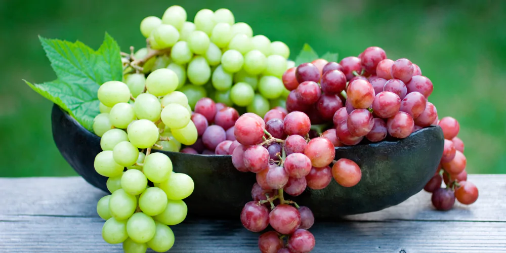 A picture of a bowl of green and red grapes on a table