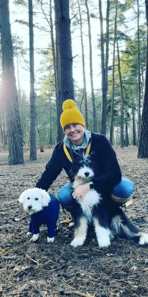 A picture of a 3 month old Bernedoodle puppy in the woods with its sibling and owner